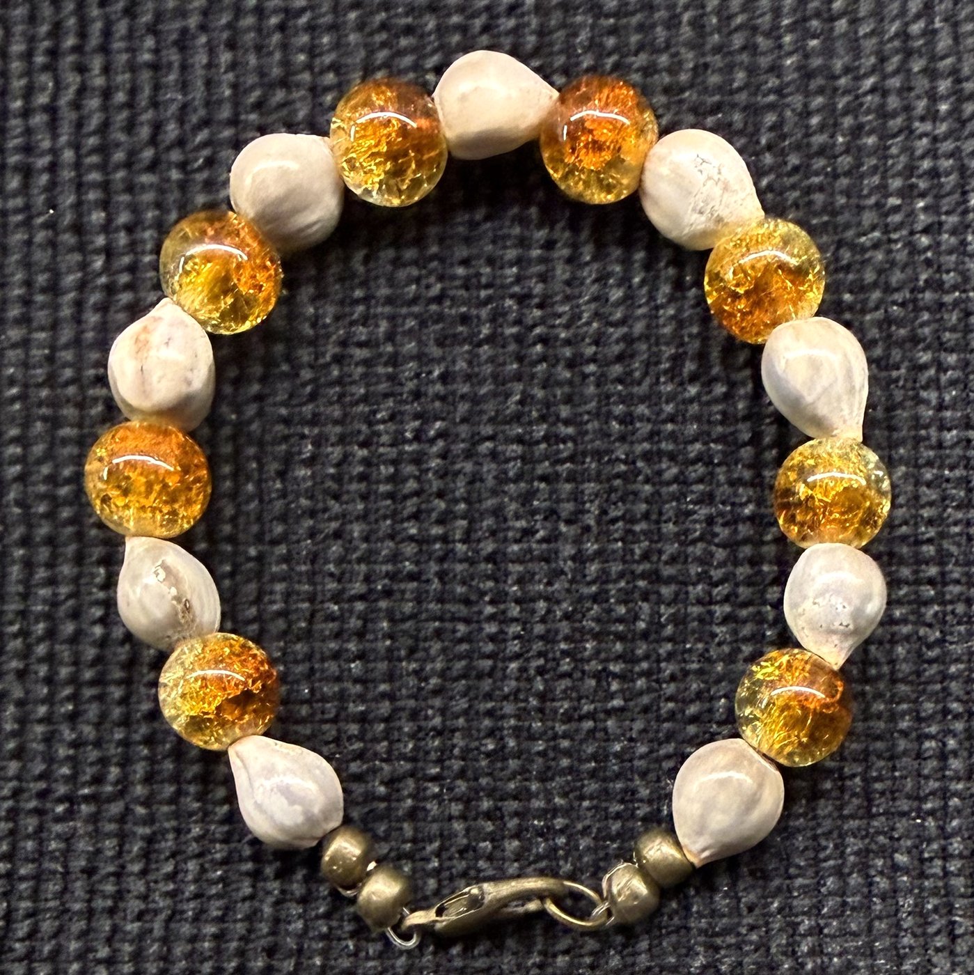 Bracelet 5, Cornmeal, 6.5": amber and golden-orange crackle glass beads alternating with grey-white Job's tears seeds and a bronze clasp.